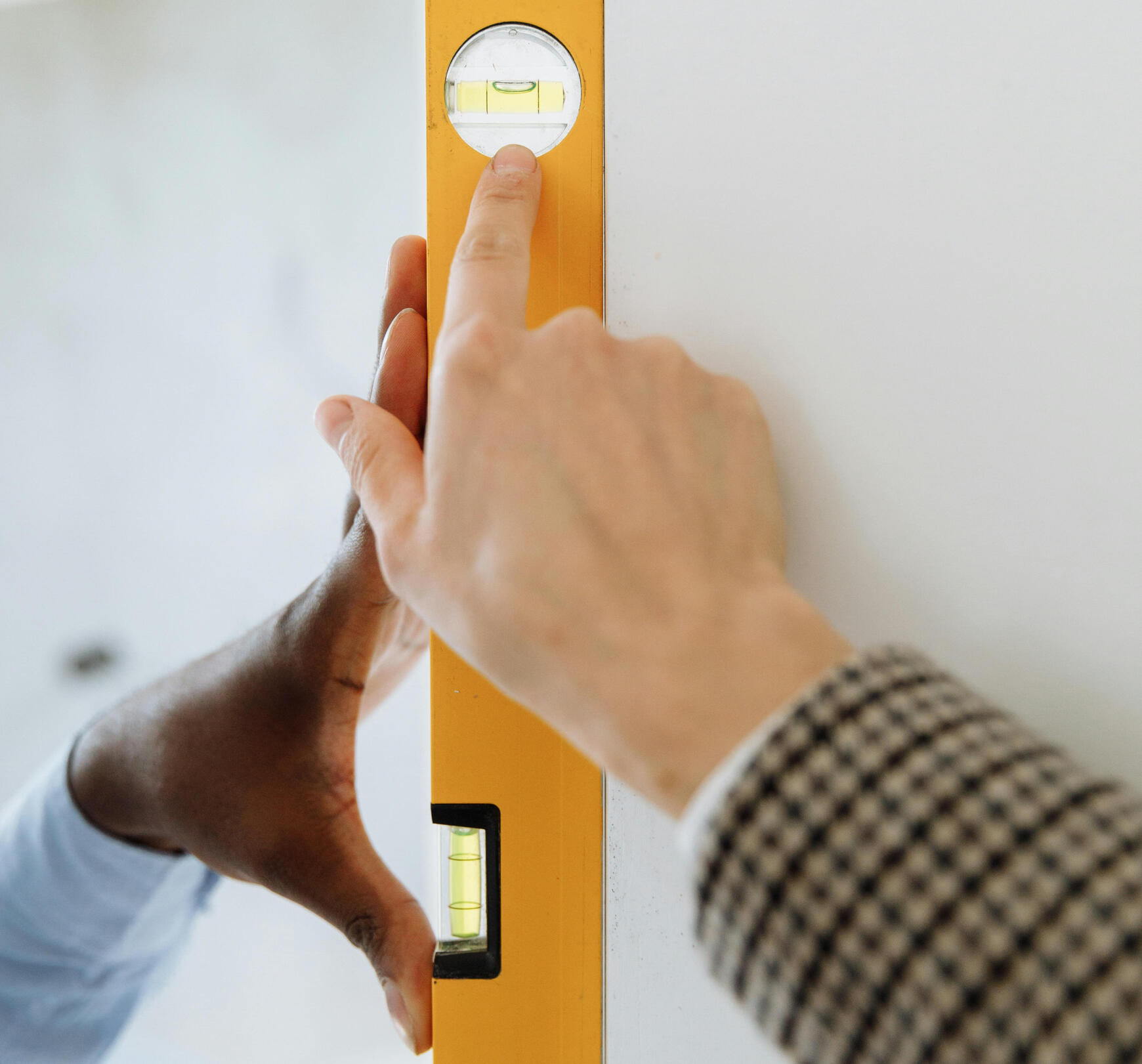 Our Value Image An image displaying a bubble level meter. One hand is holding the meter against the wall. Another is pointing towards the bubble.